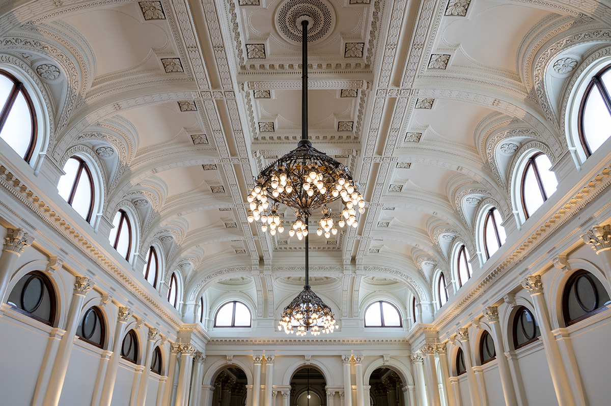 A ceiling of a white hall with arches and two large chandeliers.